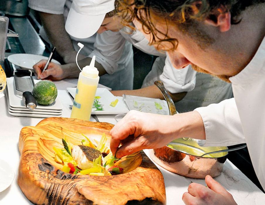 Arnaud Donckelle dressant un plat dans une assiette en bois d'olivier